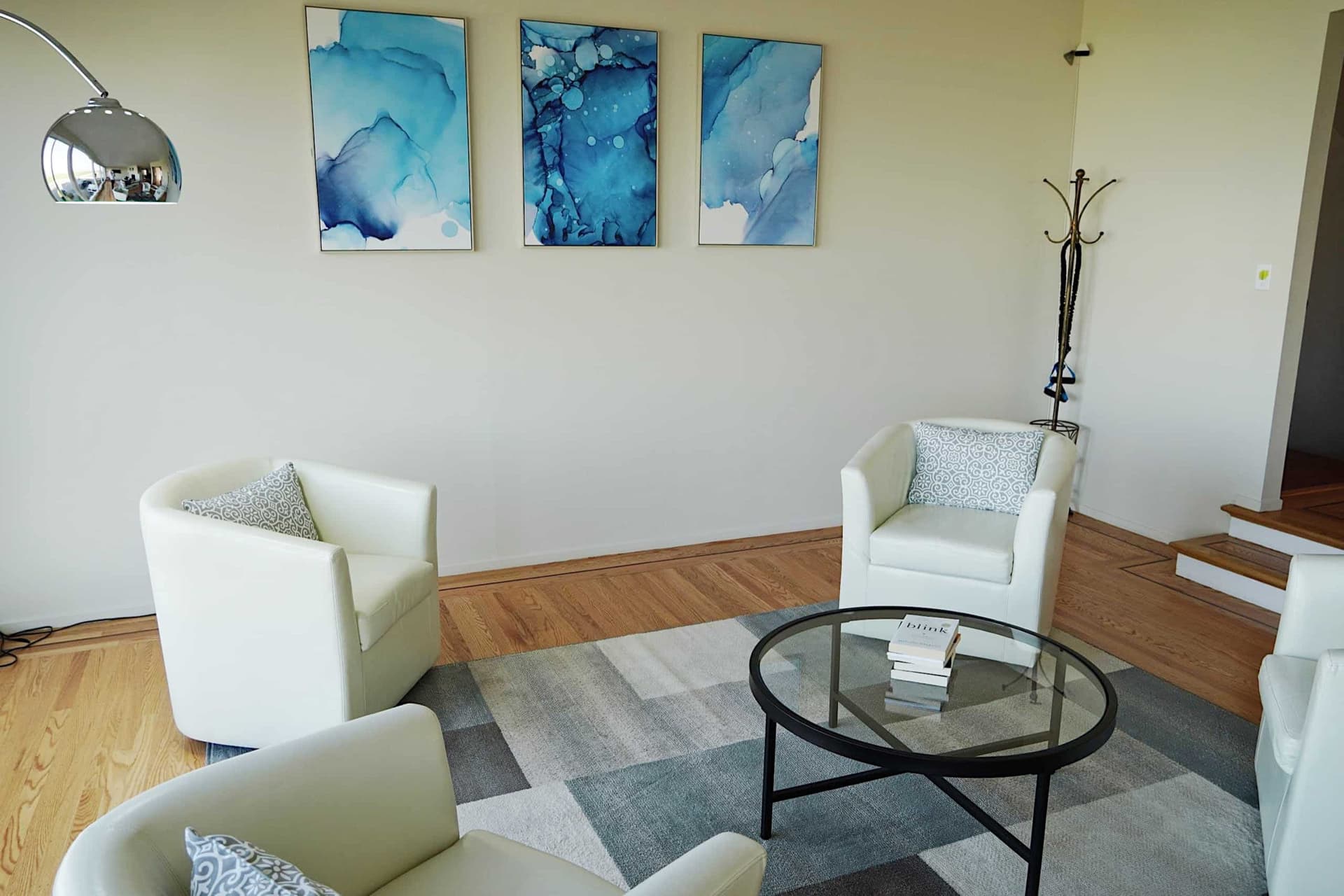 Sitting area with white armchairs, a glass coffee table and blue abstract art